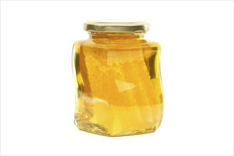 A glass jar with a golden lid contains honey with honeycomb filled almost to the top, against a