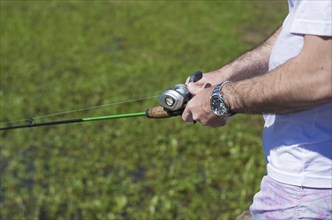 Young man fishing in pond, lake, closeup of fishing rod and reel