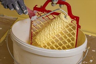 Paint roller on scraper grid in bucket with wall paint, painting work