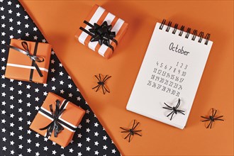 Calendar sheet for month October with Halloween spiders and gift boxes on orange and black