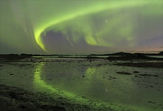 Northern lights (aurora borealis) cover the sky and are reflected in the water of a fjord,