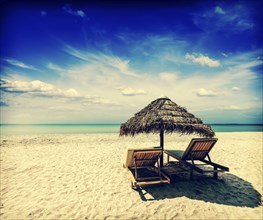 Vintage retro effect filtered hipster style image of two beach lounge chairs under tent on beach.