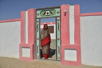 Nubian woman in typical bright dress, in front of her house, in the village of Umogaal in Dongola,