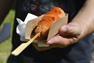 Hand holding Korean style corn dog coated in crispy panko breadcrumbs with hot sauce