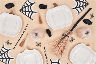 Beige Halloween party flat lay with pumpkin shaped plates, witch broom, spiders and coffins