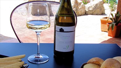 A glass of white wine with the accompanying bottle and snacks on an outdoor table, Sicilian wine,