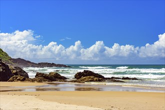 Beach with waves breaking against the rocks on a sunny day in the town of Serra Grande on the coast