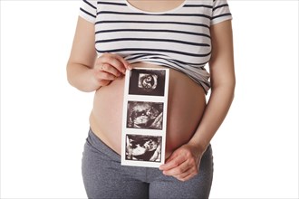 Pregnant woman standing and holding her ultrasound baby scan picture isolated on white