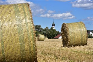 Straw bales on a harvested grain field, in the background the village church with onion tower,