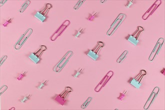 Stationery items like paper clips and drawing pins arranged on pink background