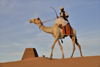 Man riding a dromedar in front of a pyramid of the northern cemetery of Meroe, Nubia, Nahr an-Nil,