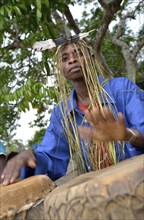 Musician with a headdress made of bast and a feather, playing drums, Nkala, Bandundu Province,