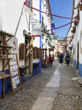 Picturesque alley with shops and pedestrians, tourists in the medieval village of Óbidos, Portugal,