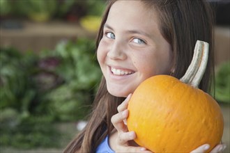 Happy young blue eyed girl holding a fresh pumpkin at the farmers market