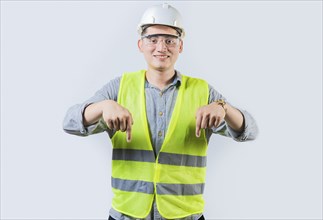 Smiling engineer pointing advertising down isolated. Smiling friendly engineer pointing down