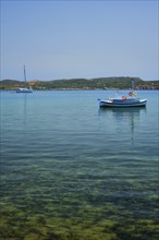 Greek fishing boat moored in blue waters of Aegean sea in harbor of near Milos island, Greece,