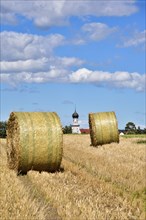 Straw bales on a harvested grain field, in the background the village church with onion tower,