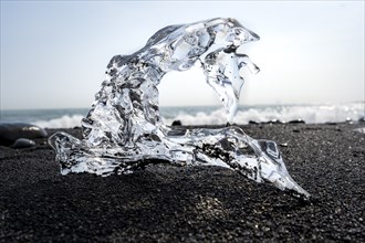 Ice, piece of ice with hole on black sand beach, on black lava beach Diamond Beach, Southeast