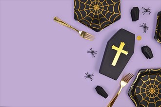 Halloween party flat lay with spider web plates, coffins, confetti and spiders on violet background