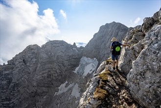 Mountaineer on a rocky narrow mountain path, view of rock faces with blue ice glacier and summit of