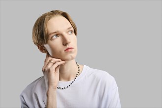 Closeup portrait of pensive young man in white t-shirt over grey studio background