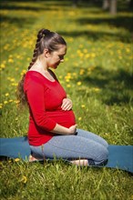 Pregnancy yoga exercise, pregnant woman doing asana Virasana Hero Pose on knees outdoors on grass