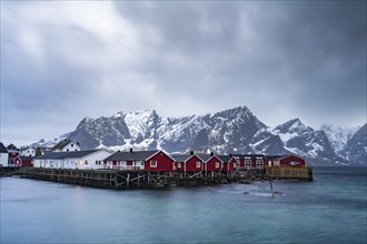 Rorbuer cabins of Hamnoy by the fjord, snowy mountains in the back, Hamnøy, Reine, Moskenesøya,