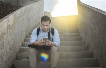 Handsome man sitting on stairs using smart phone, Front view of guy sitting on stairs using his