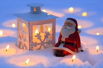 Santa Claus and lantern in the snow, with burning candles