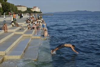 Visitors basking in the evening sun at the Sea Organ by architect Nikola Bašic, Zadar, Dalmatia,