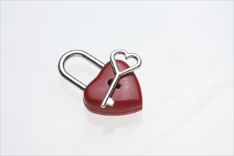 Small heart-shaped key lies on a red padlock