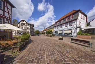 Brown street with half-timbered houses, benches and restaurant under blue sky with cumulus clouds