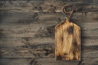 A beautifully crafted wooden cutting board rests on a dark, weathered wooden table, showcasing its