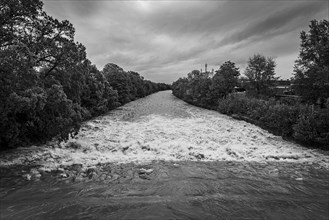 A powerful river with a strong current under a cloudy sky, surrounded by green trees, Schwarza,