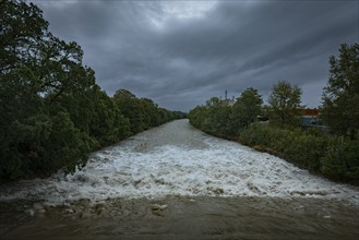 A powerful river with a strong current under a cloudy sky, surrounded by green trees, Schwarza,