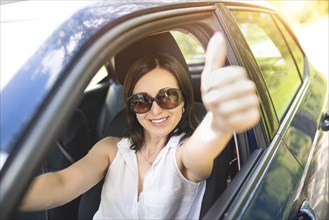 A smart looking middle-aged adult woman wearing sunglasses put her hand out the car window and