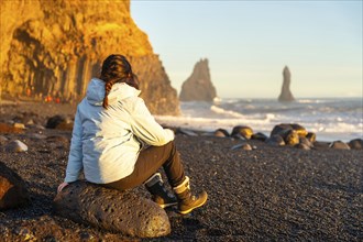 Female hiker sitting on the black sand beach of Reynisfjara looking at the sea. Iceland