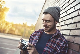 Smiling man with retro photo camera Fashion Travel Lifestyle outdoor while standing against brick