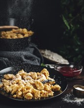 Kaiserschmarrn on a black plate, sprinkled with sugar, dark background