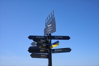 Black signpost against a blue sky with directions to various towns and destinations, Fløibanen