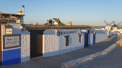 Building with white-blue walls and restaurant sign in a rustic landscape, windmills in the