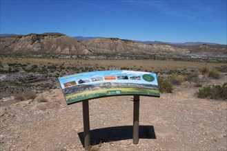 Viewpoint with an information board in a desert landscape with mountains and a clear sky, Llano de