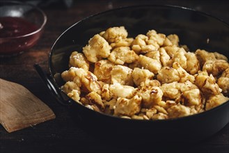 Kaiserschmarrn in a pan, close-up with brown wooden spoon and jam on a dark background