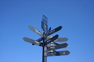 Black signpost against a blue sky with directions to various towns and destinations, Fløibanen