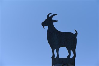 Silhouette of a metallic goat statue in front of a clear blue sky, Fløibanen mountain station,