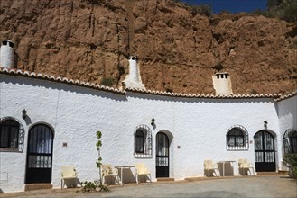 White building with arches and chairs in front of a rock face, under a sunny sky, Pedro Antonio de