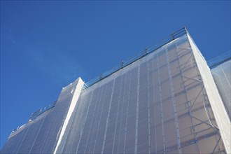 Shielding of a building by a tarpaulin attached to scaffolding against a clear blue sky, Bergen,