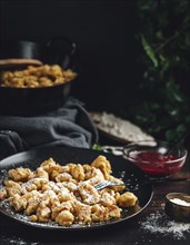 Kaiserschmarrn on a black plate sprinkled with sugar, pan in the background, dark surroundings