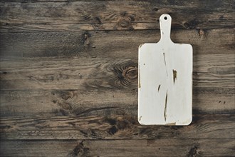 A well-worn wooden cutting board rests on a dark, rustic wooden table. The board shows signs of use