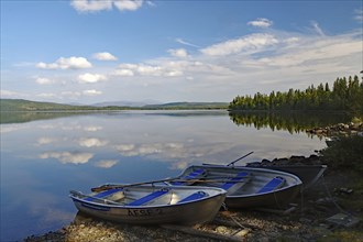 A calm lake with two docked boats, surrounded by trees and a slightly cloudy sky, Viken, Störlien,